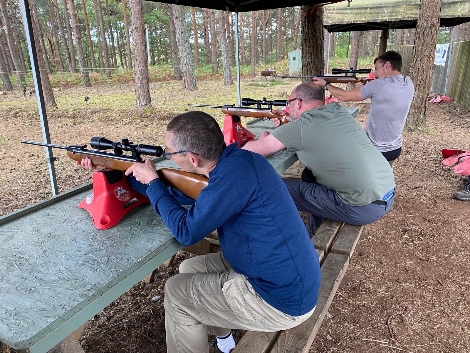 Three shooters at the covered .22 rifle range with scoped rifles resting on supports