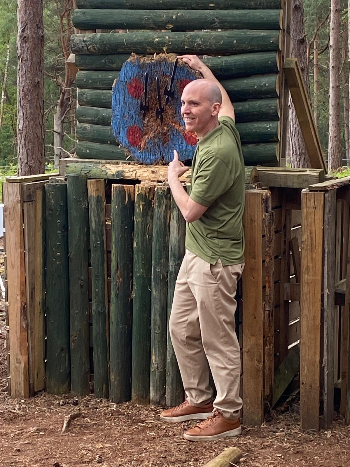 Participant beside a timber target with axes embedded in the bullseye