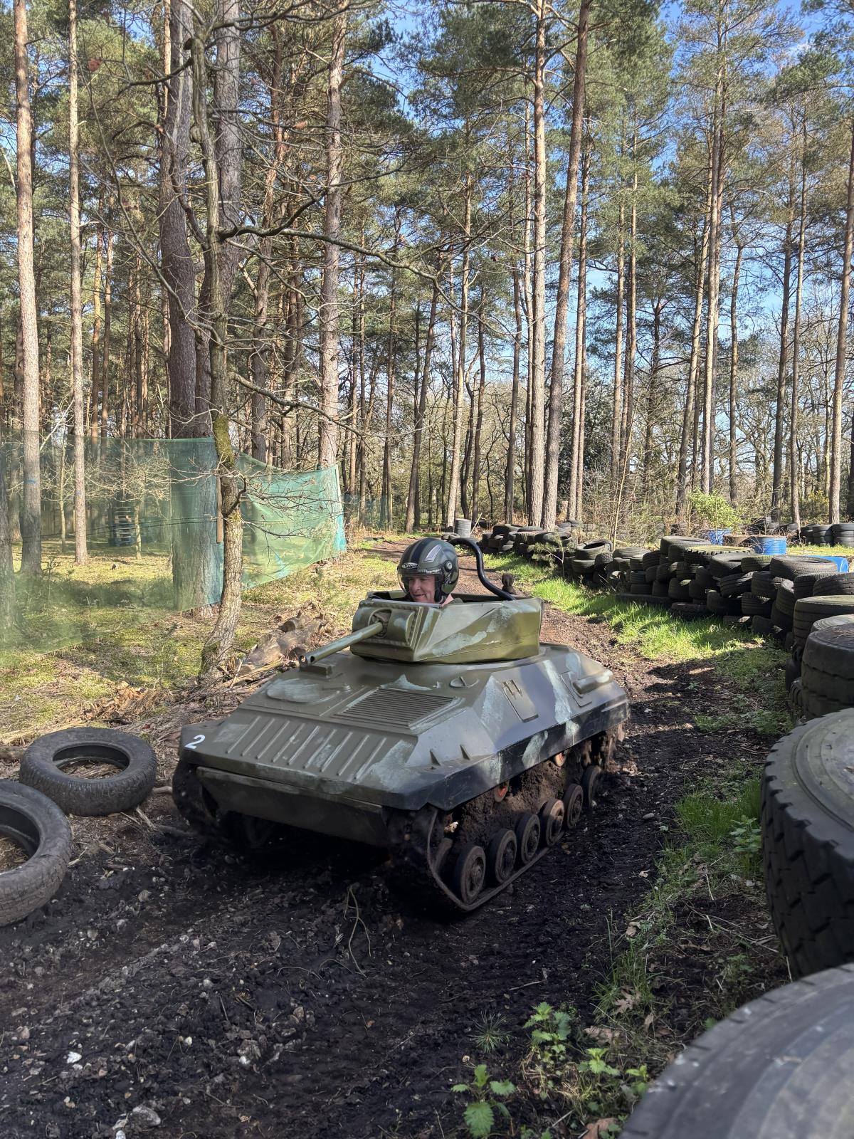 Driver in a helmet steering a one-person mini tank along a woodland track